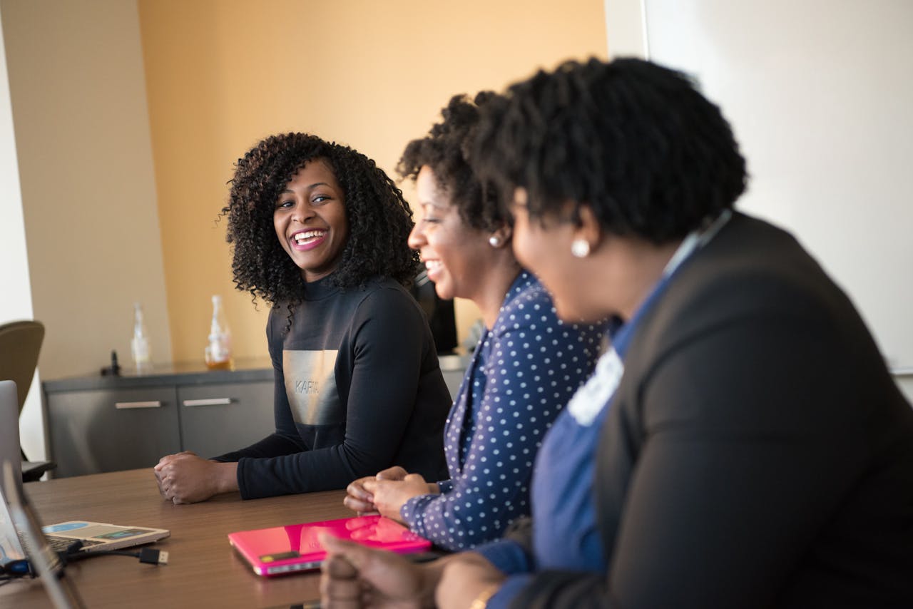 Three black women in a happy office meeting, engaging in teamwork.
