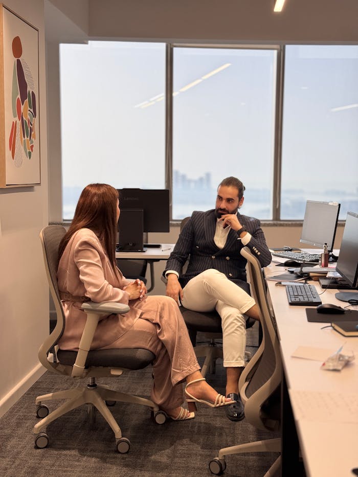 Two professionals in a modern office, discussing business strategies by large windows.