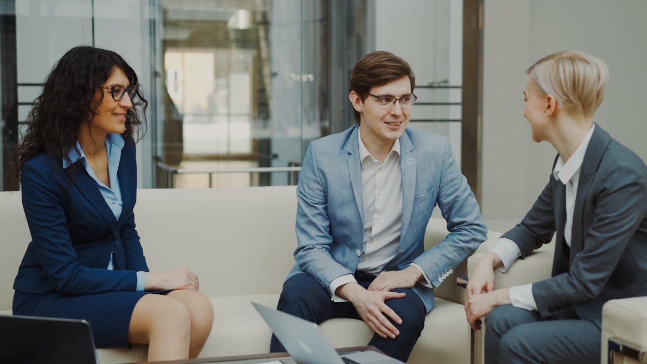 Three business professionals engaged in a discussion in a modern office setting, wearing suits.