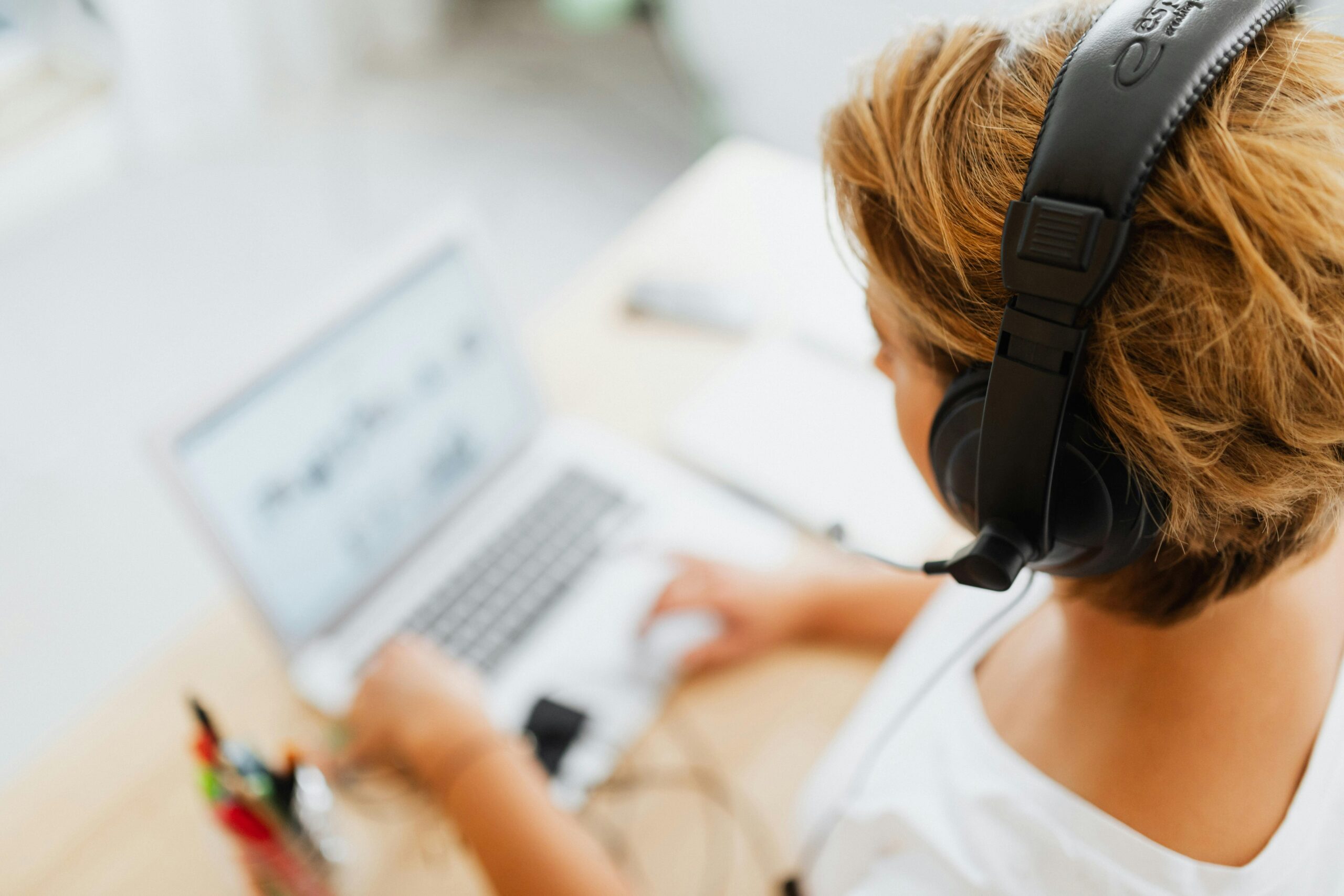 A woman working on a laptop with headphones in a bright indoor setting, embodying remote work and digital lifestyle.