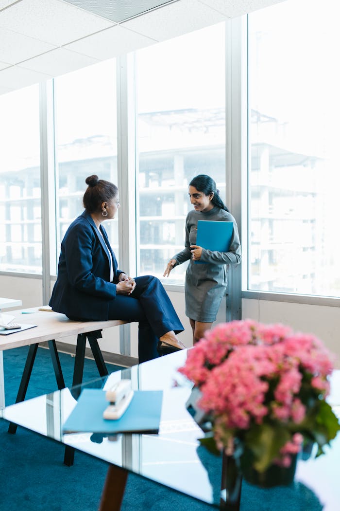 Two professional women in business attire having a conversation in a modern office setting.