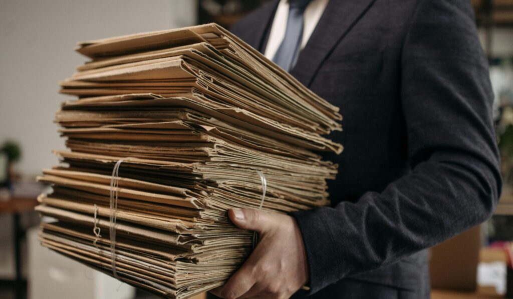 Capital Group Close-up of business professional holding a large stack of brown folders in an office setting.