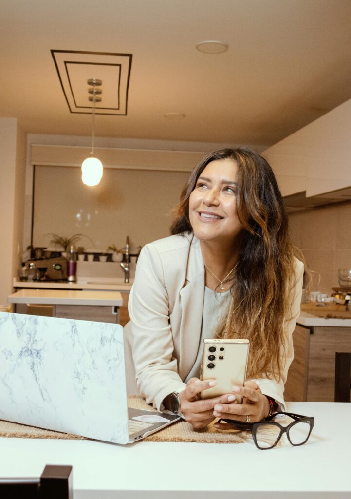 Happy woman holding phone in a modern kitchen setting, illustrating a casual lifestyle.